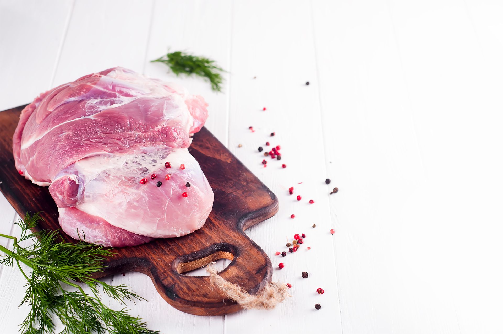 Rohes Fleisch auf einem Holzschneidebrett, umgeben von frischen Kräutern und Gewürzen.