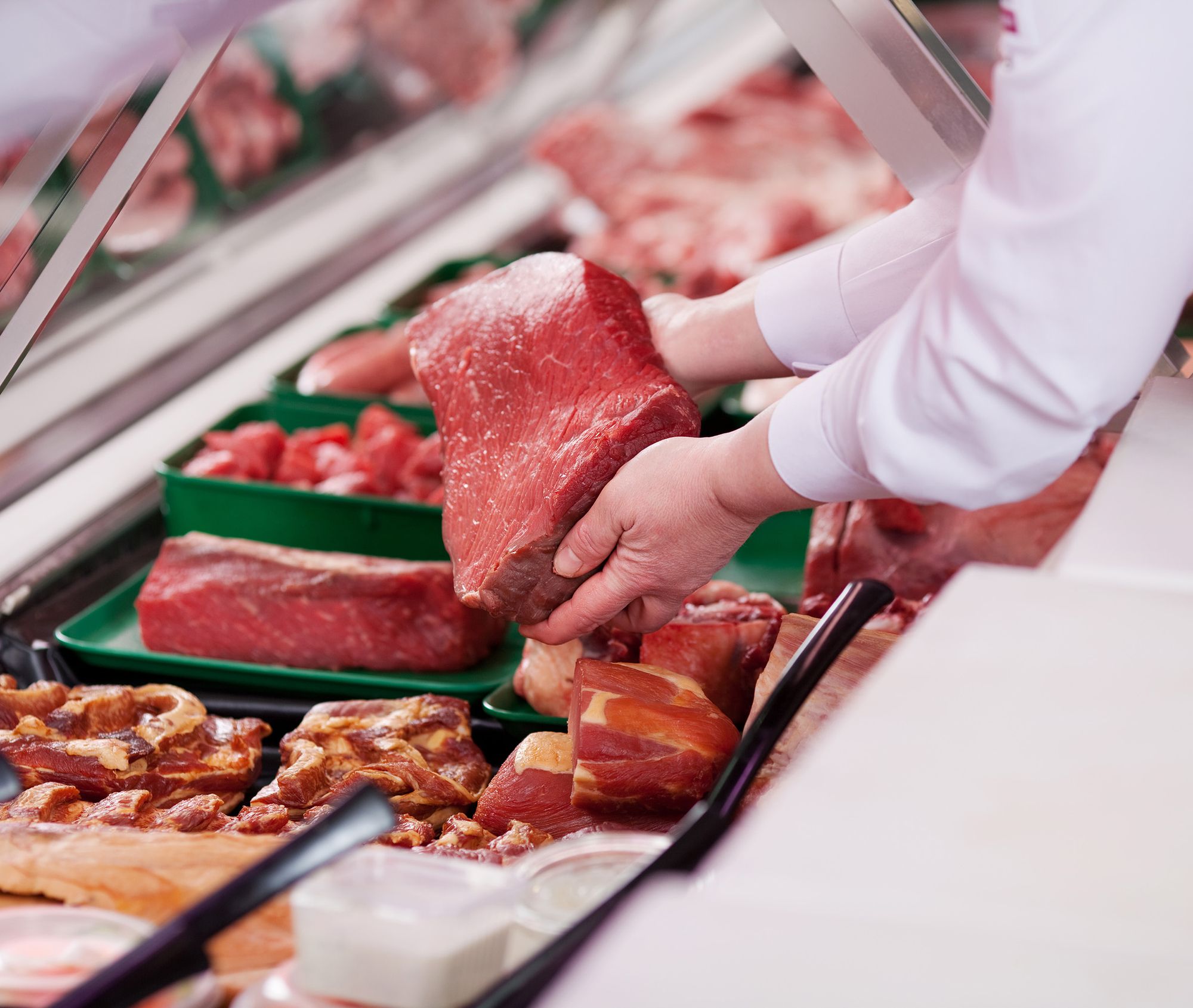 Eine Person hebt Fleisch aus einer Fleischvitrine.