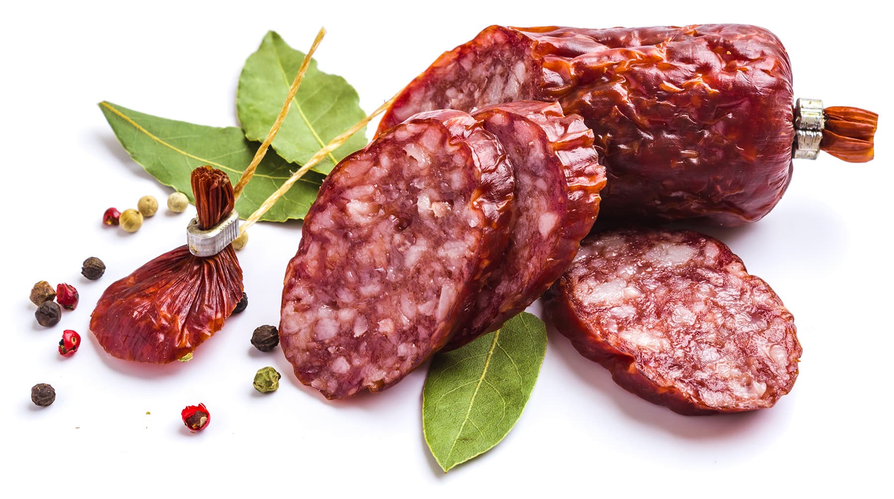 In Scheiben geschnittene Salami, gewürzt und umgeben von frischen Kräutern.